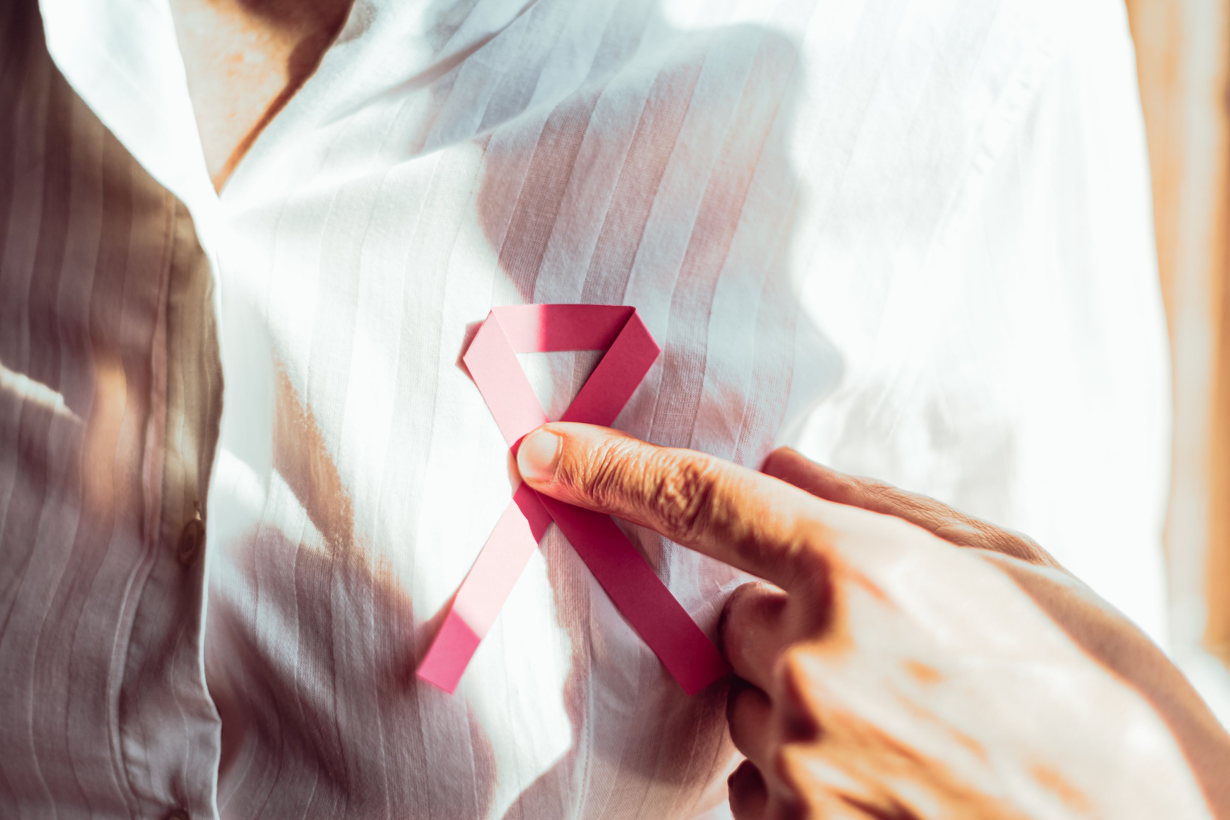 close-up-of-a-person-holding-a-pink-ribbon-on-their-chest.jpg